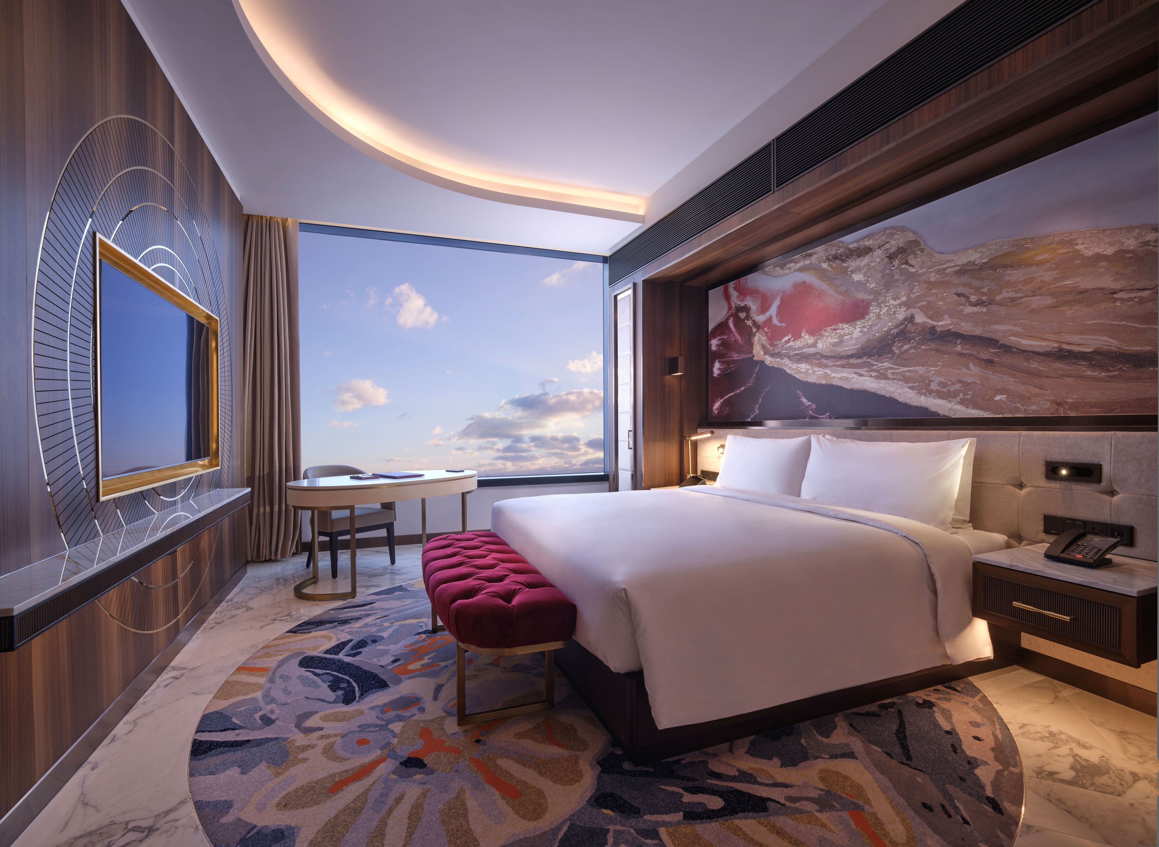 A modern hotel room with a large bed, a desk, and a view of the sky.