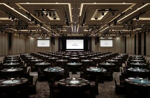 A conference room with multiple tables set for dining, a large screen at the front, and overhead lighting. - Inspire Entertainment Resort (Incheon)
