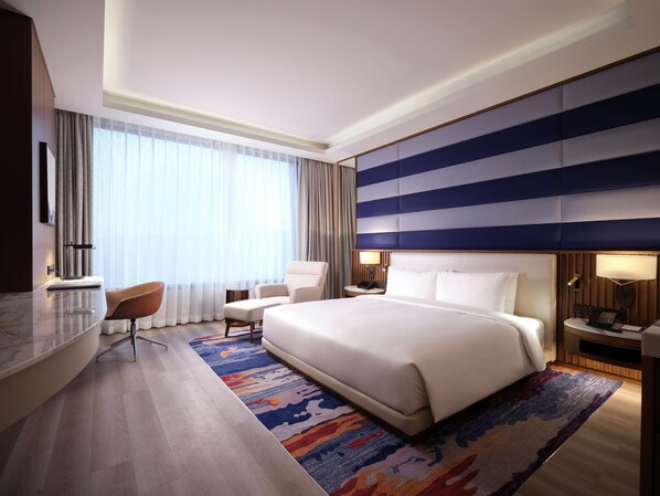 A modern hotel room with a large bed, a desk, a chair, and a view of the city through large windows. - Inspire Entertainment Resort (Incheon)