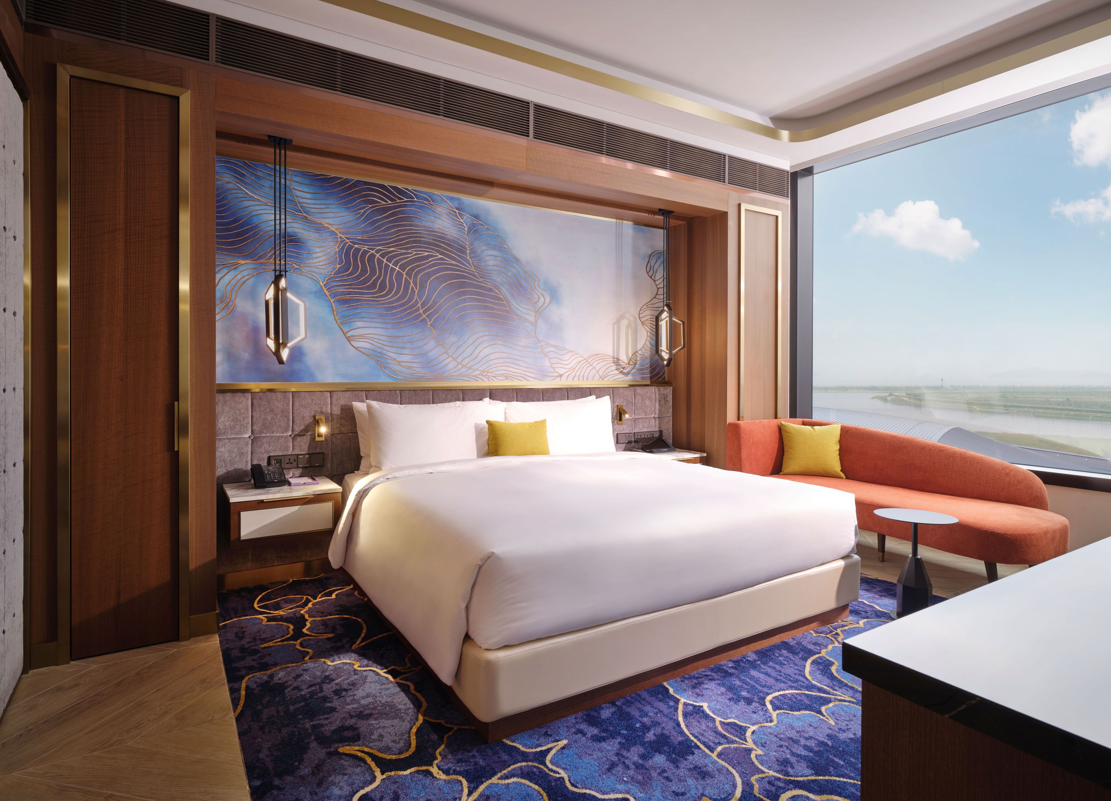 A hotel room with a large bed, a sofa, a nightstand, a lamp, and a view of the sea.