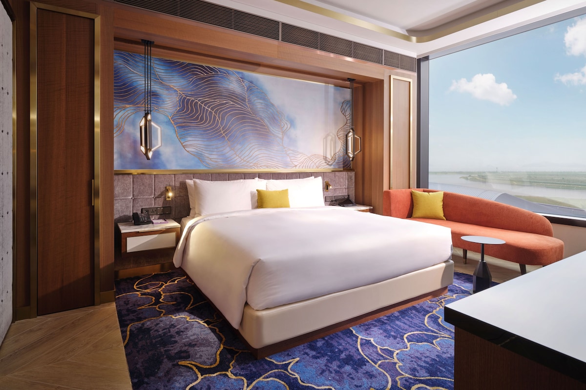 A hotel room with a large bed, a nightstand, a desk, and a view of the sea.