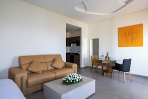 A modern living room with a sofa, coffee table, and dining area. - Le Tanger By Mnar Palm (Al Bahraoyine)