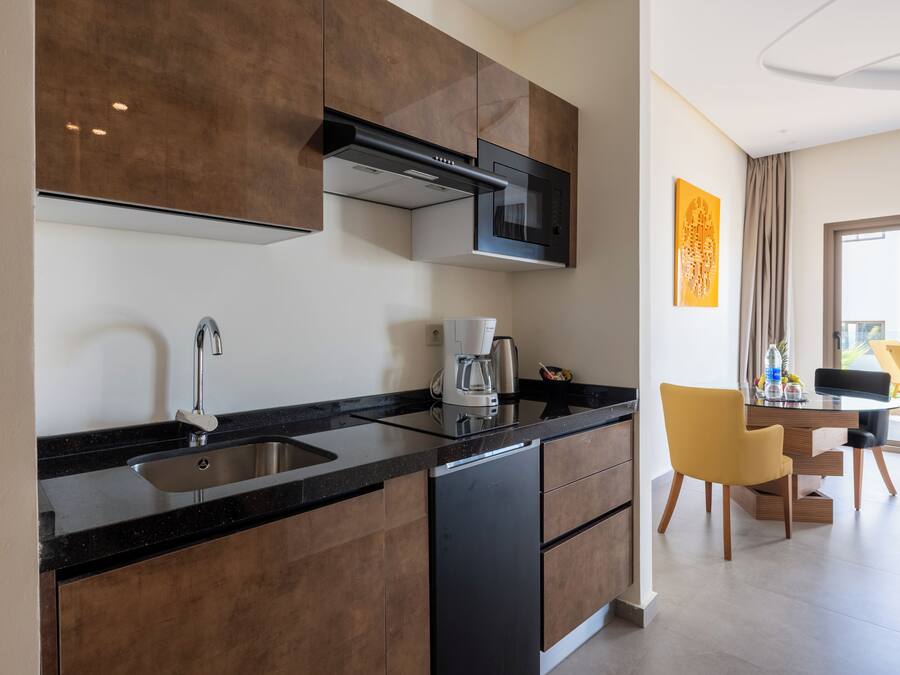 A modern kitchen with a built-in microwave, coffee maker, and sink. There is a dining area with a table and chairs visible in the background.