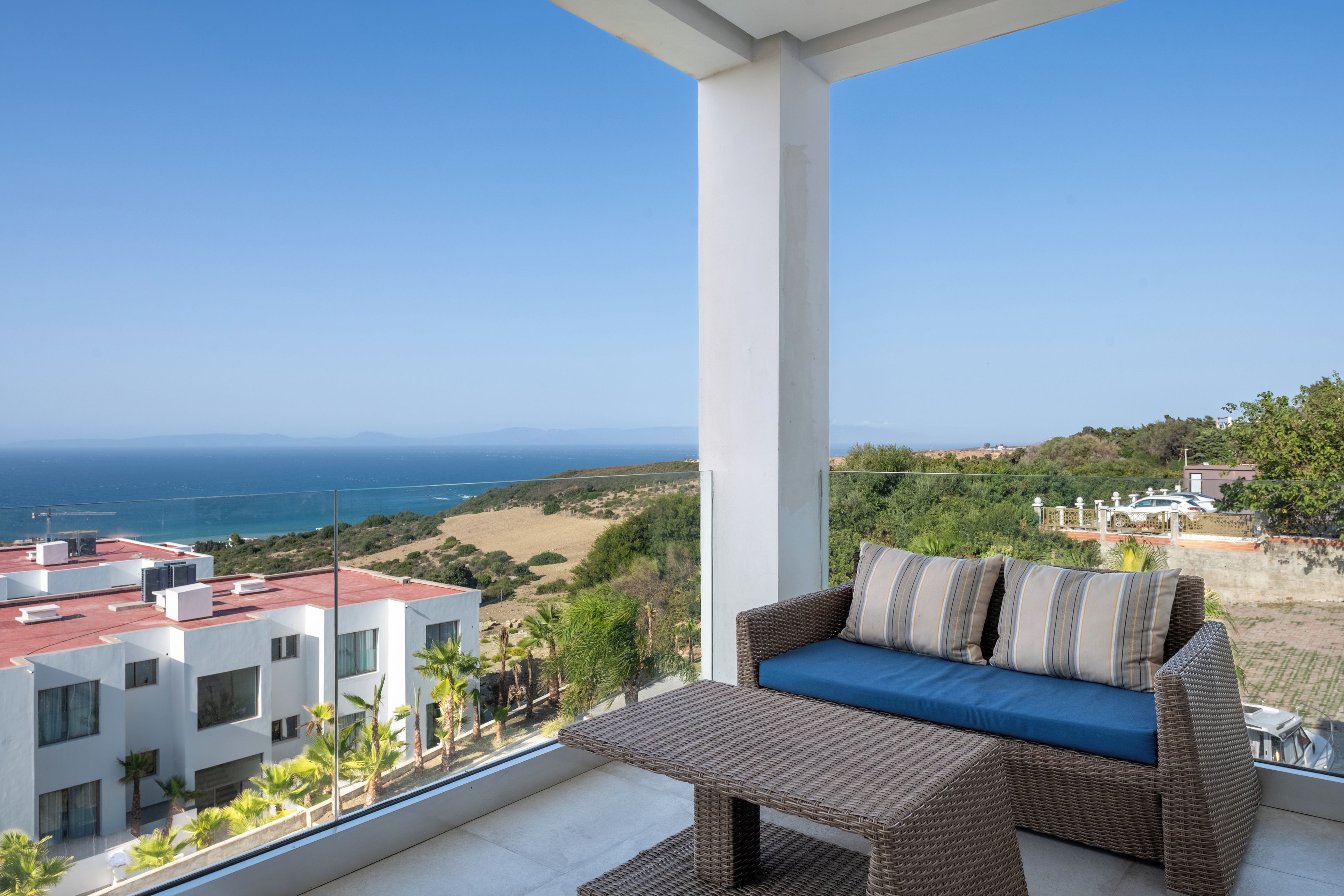 Un balcone con un divano in vimini e vista sul mare e sul paesaggio.