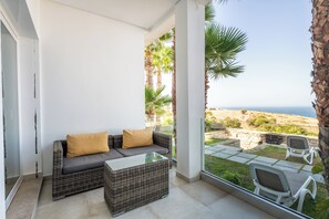 A balcony with wicker furniture, a glass table, and a view of the sea. - Le Tanger By Mnar Palm (Al Bahraoyine)