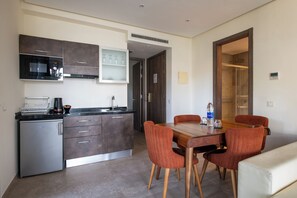 A compact kitchen with a microwave, stove, and a small refrigerator. There is a dining table with four chairs and a bench. - Le Tanger By Mnar Palm (Al Bahraoyine)
