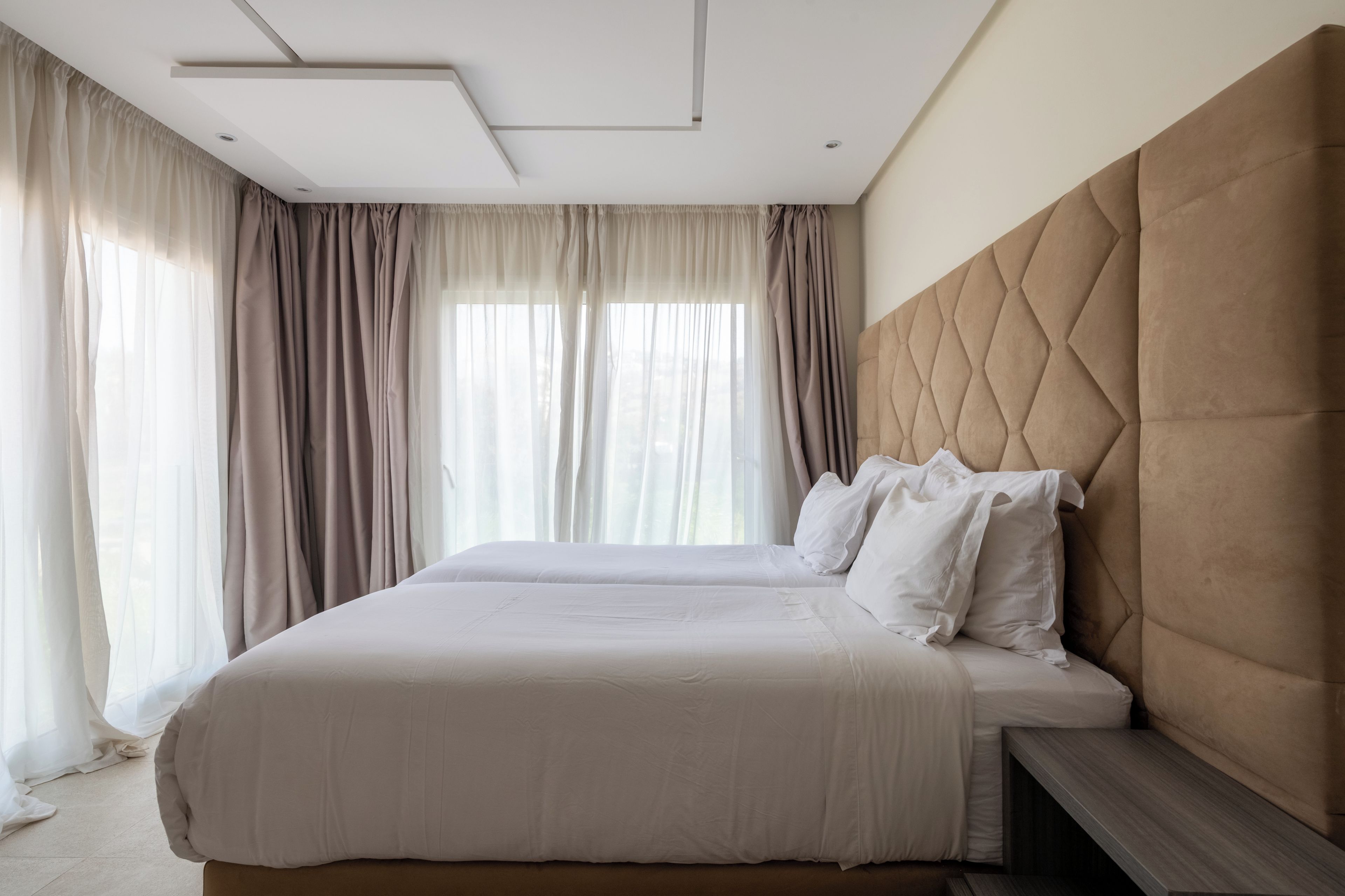 A hotel room with a large bed, a headboard, and a window with curtains.