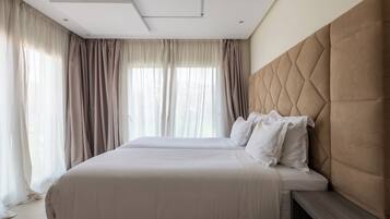 Una habitación de hotel con una cama grande, cabecera y ventana con cortinas.
