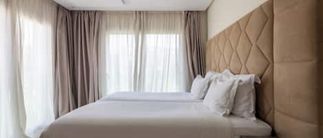 A hotel room with a large bed, a headboard, and a window with curtains.