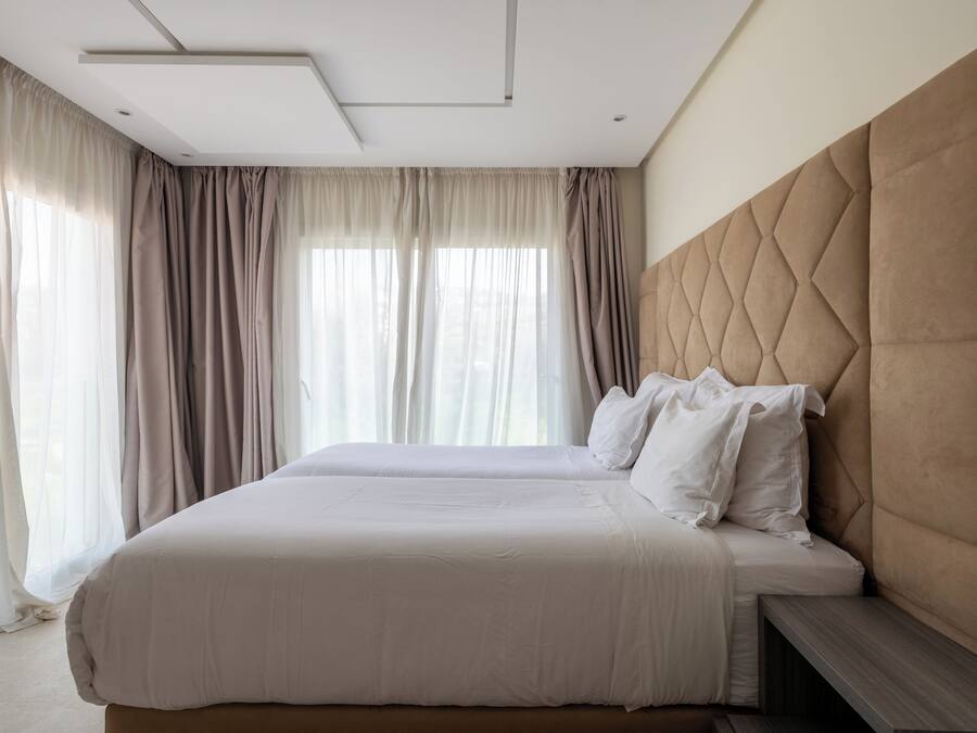 Una habitación de hotel con una cama grande, cabecera y ventana con cortinas.