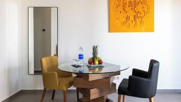 Un comedor moderno con una mesa de vidrio, dos sillas, un cuenco de frutas y una botella de agua.