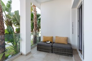 Een balkon met een rieten bank, twee kussens en een kat.