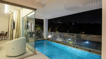 Una piscina interior moderna con paredes de cristal, una zona de estar y vistas al cielo nocturno.