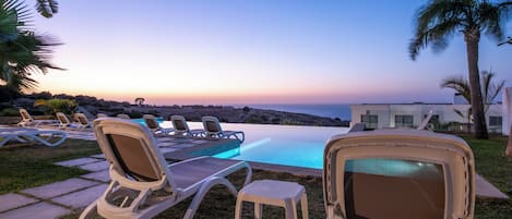 A poolside area with lounge chairs and a small pool, overlooking a scenic landscape.