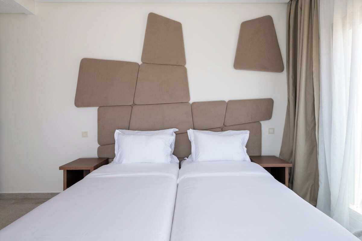 A double bed with a headboard made of geometric shapes, two bedside tables, and a window with curtains.