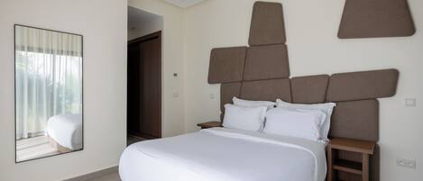 A modern hotel room with a large bed, a bedside table, and a mirror on the wall.
