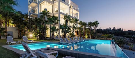 A modern hotel with a swimming pool, lounge chairs, and palm trees.