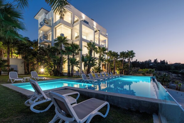 Um hotel moderno com piscina, cadeiras de lounge e palmeiras.