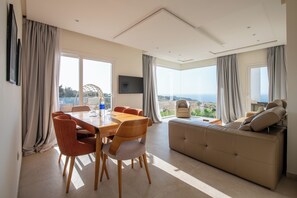 A modern living room with a large sofa, dining table, and chairs. There are large windows offering a view of the outdoors. - Le Tanger By Mnar Palm (Al Bahraoyine)