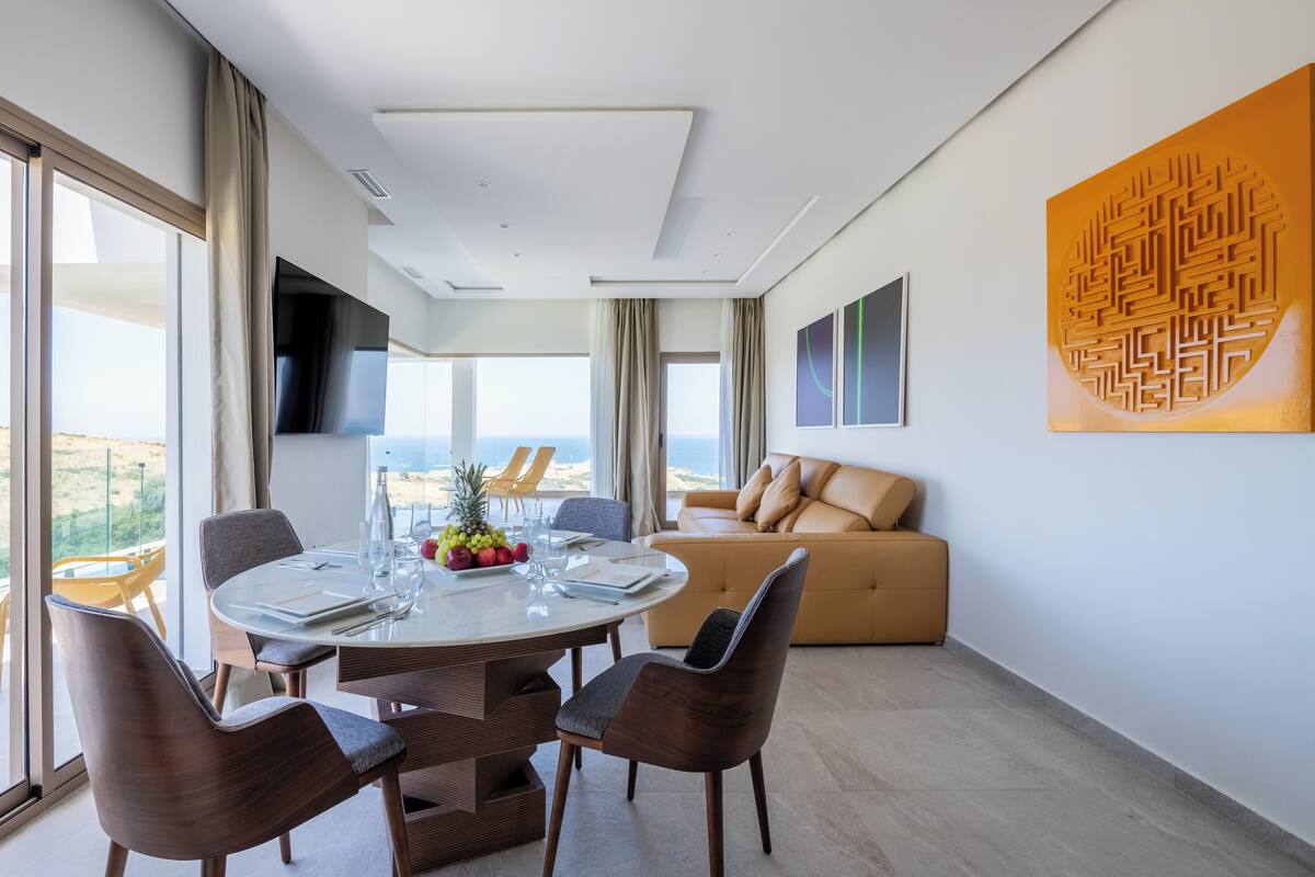 A modern dining area with a round table, chairs, and a view of the ocean.