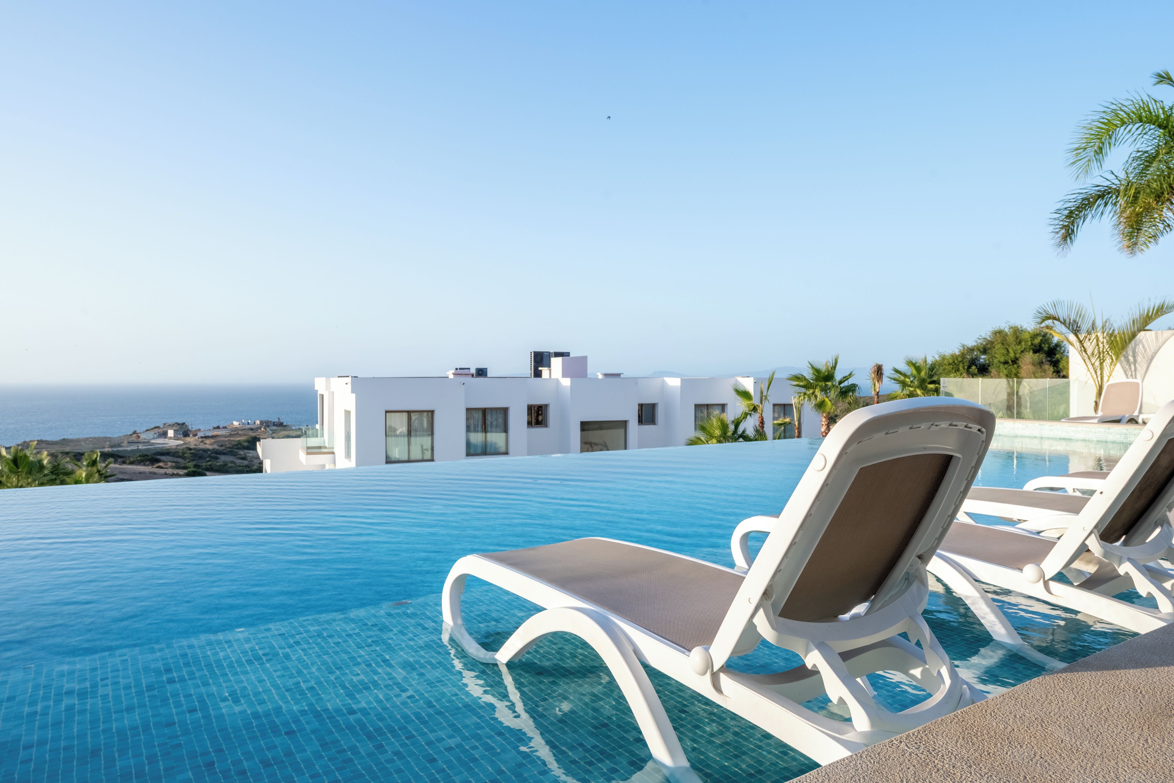 A poolside area with lounge chairs and a view of the ocean and a modern building.