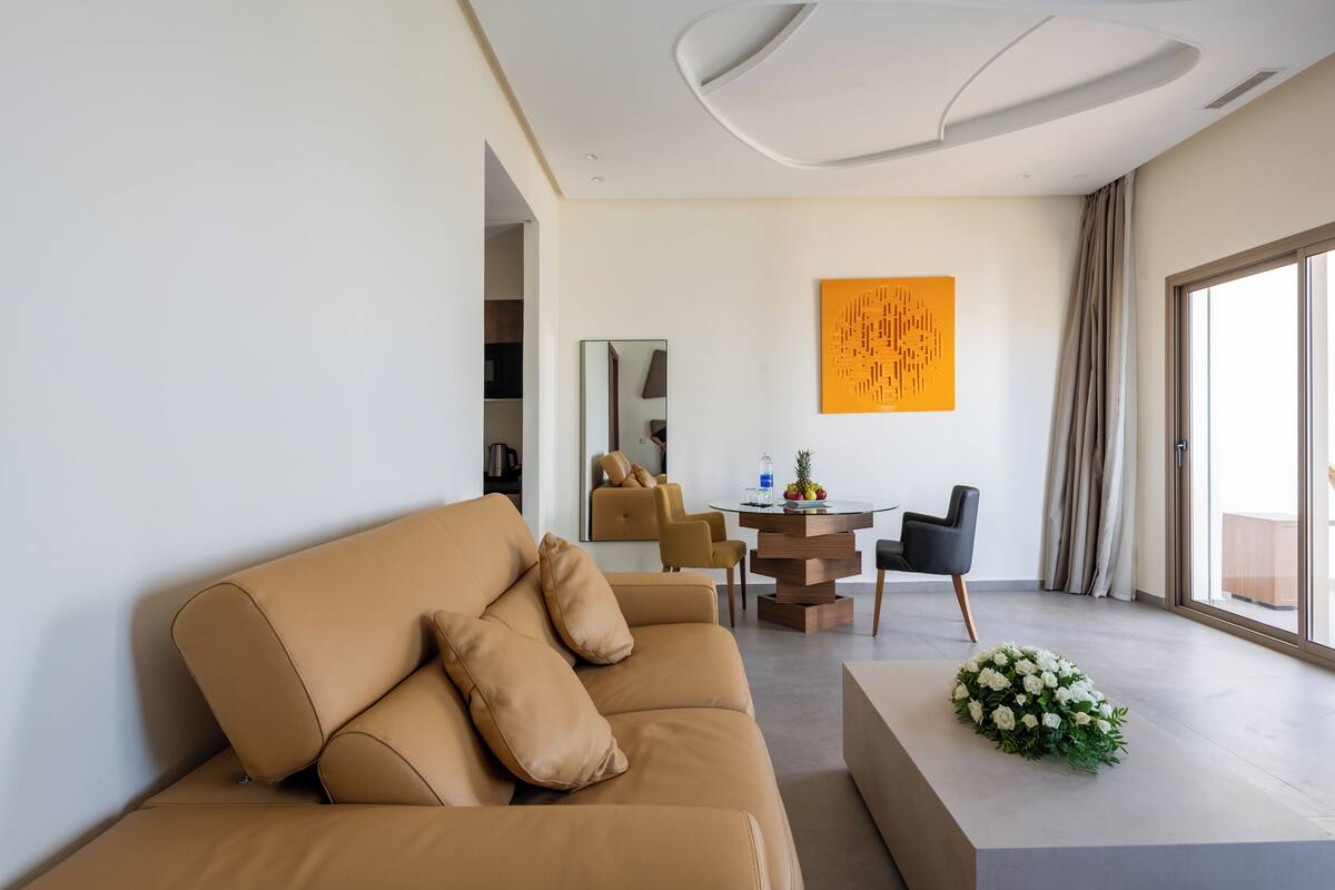 A modern living room with a tan sofa, a round coffee table, and a decorative white flower arrangement.