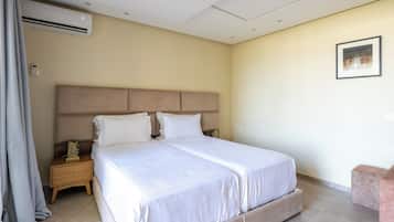 Una habitación de hotel con una cama grande, una mesita de noche, un equipo de aire acondicionado y un cuadro en la pared.