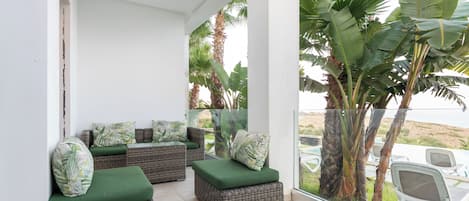A balcony with wicker furniture, green cushions, and a view of palm trees.