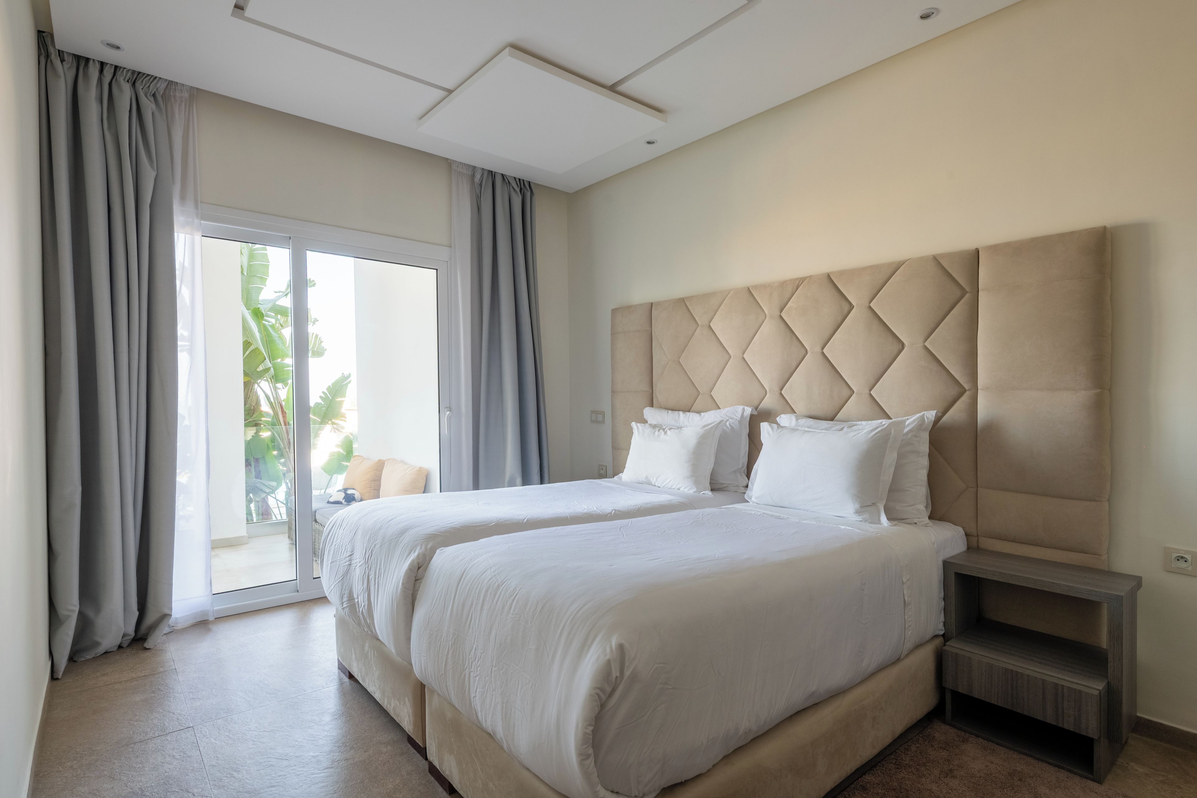 A modern hotel room with a large bed, a nightstand, and a sliding glass door leading to a balcony.
