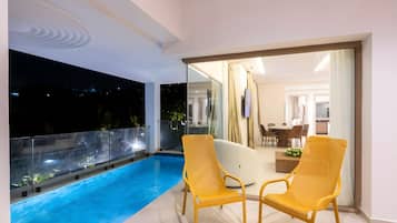 Un balcón con piscina, dos sillas amarillas y un área de comedor visible a través de una puerta de cristal.