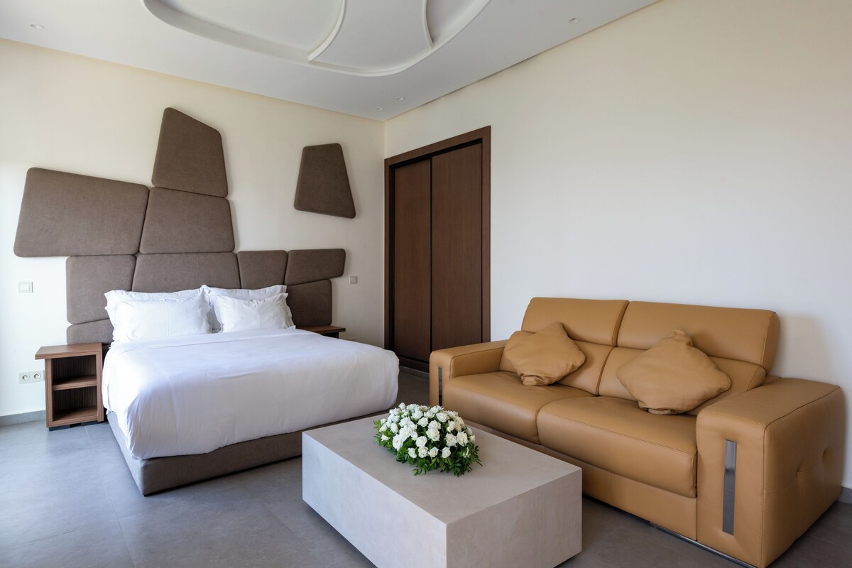 A modern hotel room with a large bed, a sofa, and a coffee table.