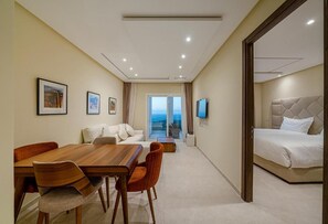 A hotel room with a large bed, a dining area with a wooden table and chairs, a sofa, and a TV mounted on the wall. - Le Tanger By Mnar Palm (Al Bahraoyine)