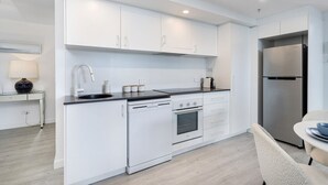 Une cuisine moderne avec des meubles blancs, un plan de travail noir, un réfrigérateur en acier inoxydable et un coin repas comprenant une chaise et une table.