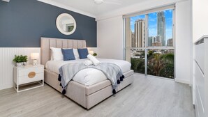 Une chambre moderne avec un grand lit, une table de chevet, un miroir rond et une vue sur la ville grâce à de grandes fenêtres du sol au plafond.
