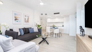 Un salon moderne avec un canapé gris, une table basse en verre et un coin repas comprenant des chaises blanches et une petite table.