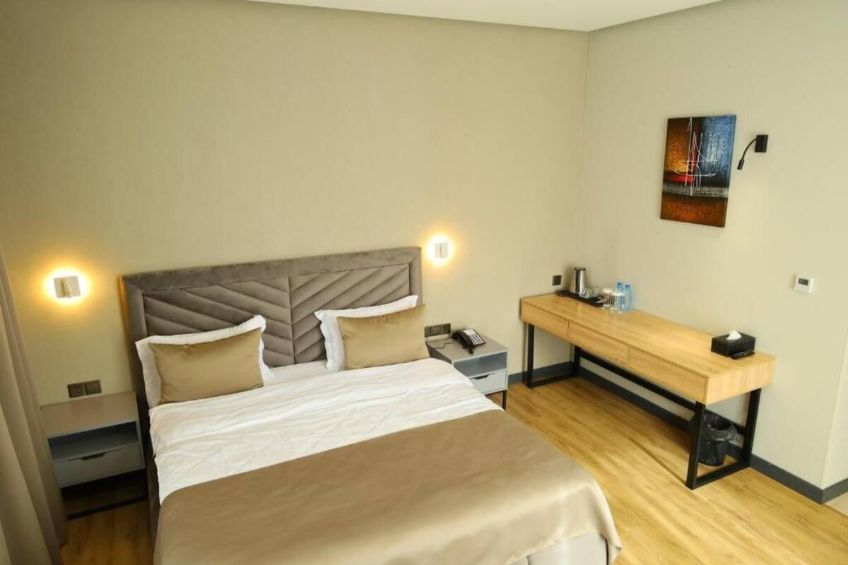 A modern hotel room with a large bed, bedside tables, a desk, and a painting on the wall.