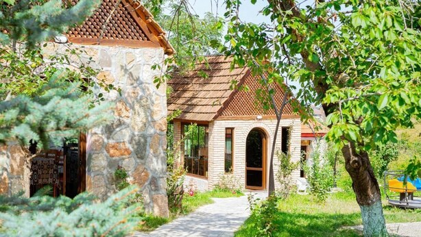 Un bâtiment en pierre avec un toit en tuiles, un chemin menant à l’entrée et un arbre au premier plan.