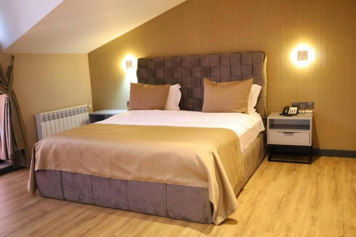 A bedroom with a large bed, a nightstand, a bedside table, and a wall-mounted light fixture.