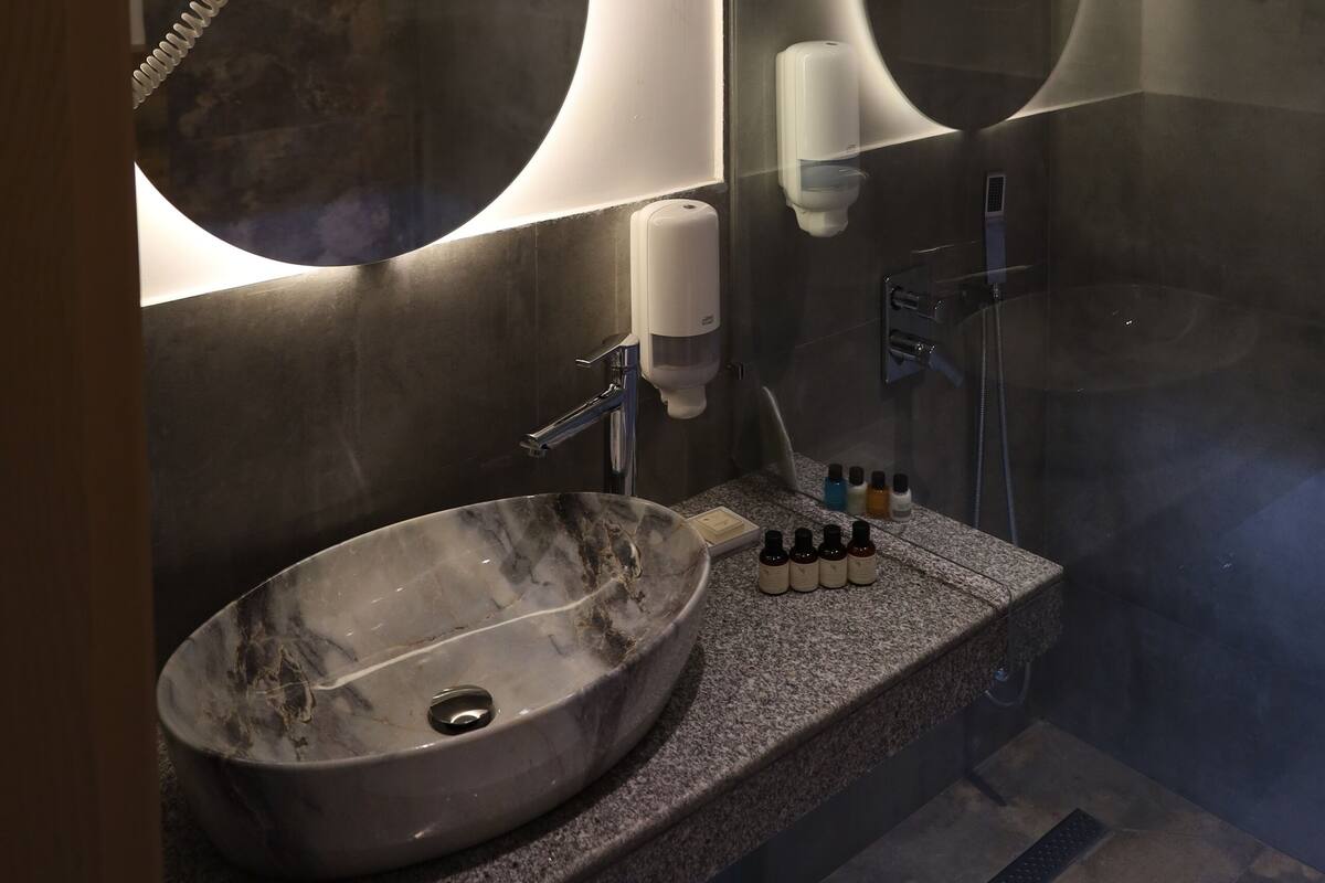 A modern bathroom with a large oval sink, a mirror, and a shower area.