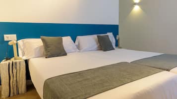 A hotel room with a large bed, two bedside tables, a nightstand, a wall socket, and a wall-mounted light.