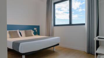 A modern bedroom with a large window, a bed with white bedding, and a blue accent wall.