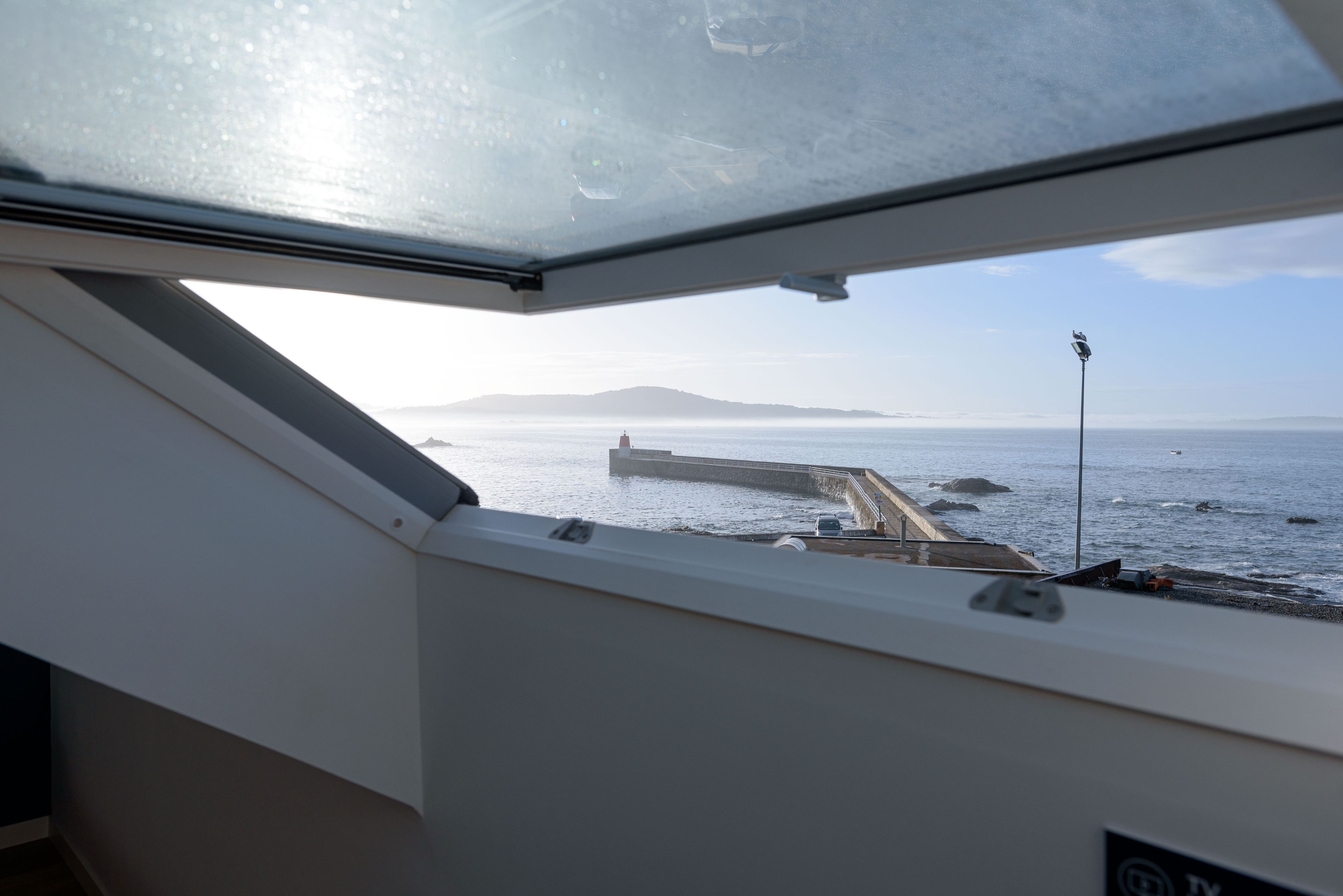 Blick aus einem Bootsfenster auf ein ruhiges Meer mit einer fernen Insel und einem Steg.