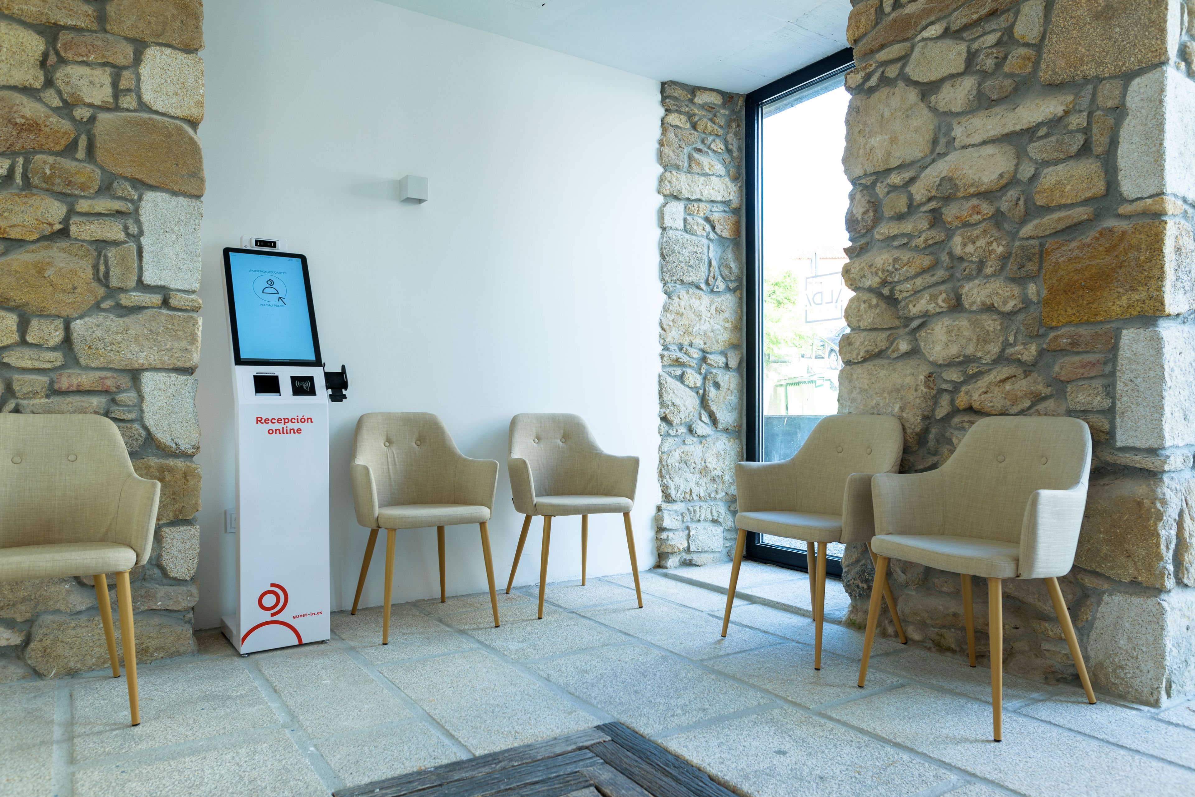 A reception area with a digital kiosk, four chairs, stone walls, and a tiled floor.