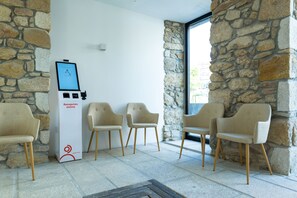 A reception area with a digital kiosk, four chairs, stone walls, and a tiled floor.