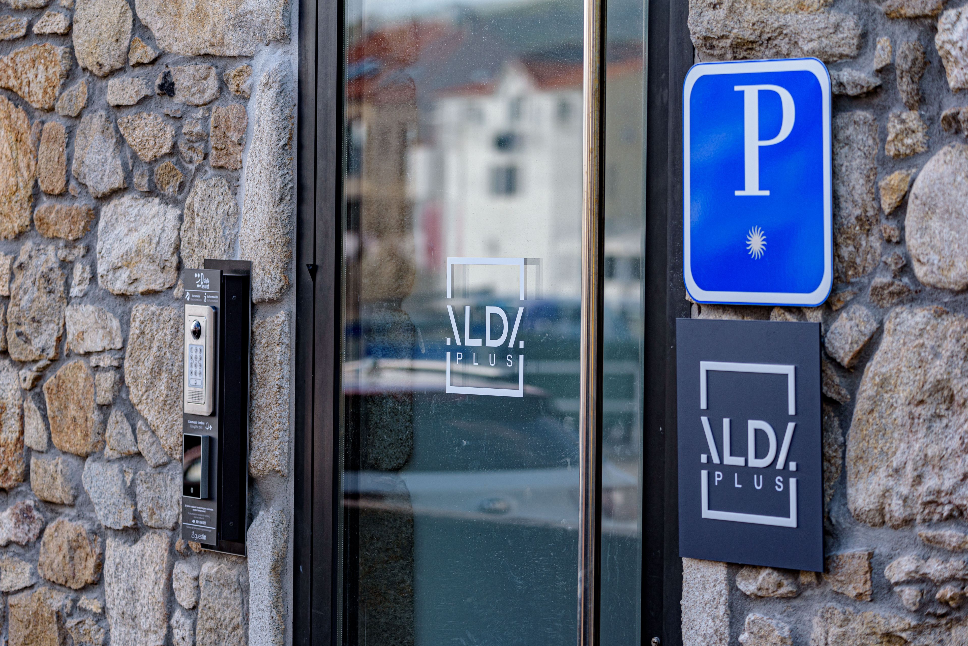 Een stenen muur met een parkeersbord en een deur voorzien van een keypad en een bord waarop 'ALDI PLUS' staat.