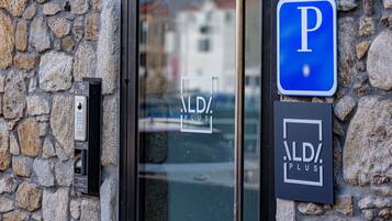 Un muro de piedra con un letrero de estacionamiento y una puerta con teclado numérico y un cartel que dice "ALDI PLUS".