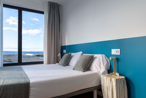 A bedroom with a large window, a bed with pillows, a bedside table, and a wall-mounted light. - Alda Corrubedo (Ribeira)