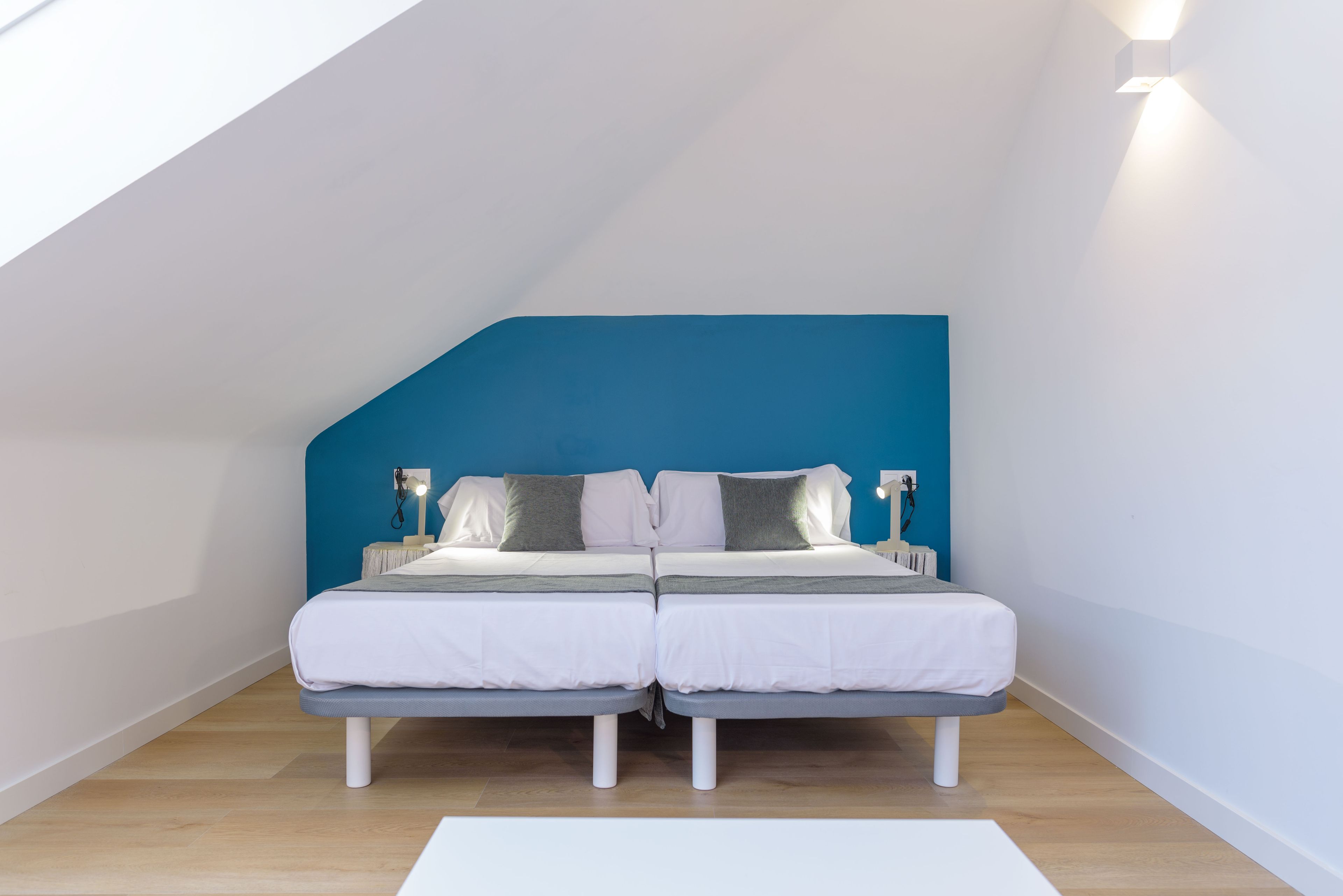 Un dormitorio con dos camas, una pared de acento azul y un tragaluz.