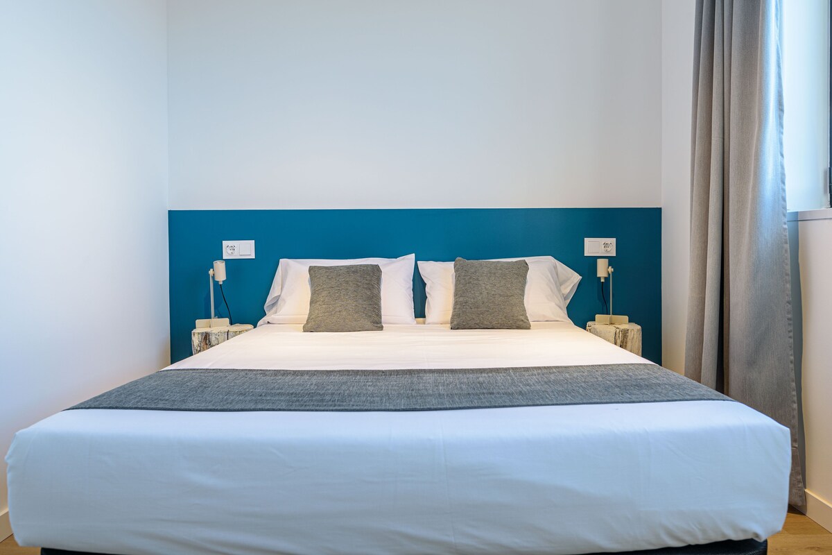 A neatly made bed with white and gray bedding, two bedside tables with lamps, and a blue accent wall.