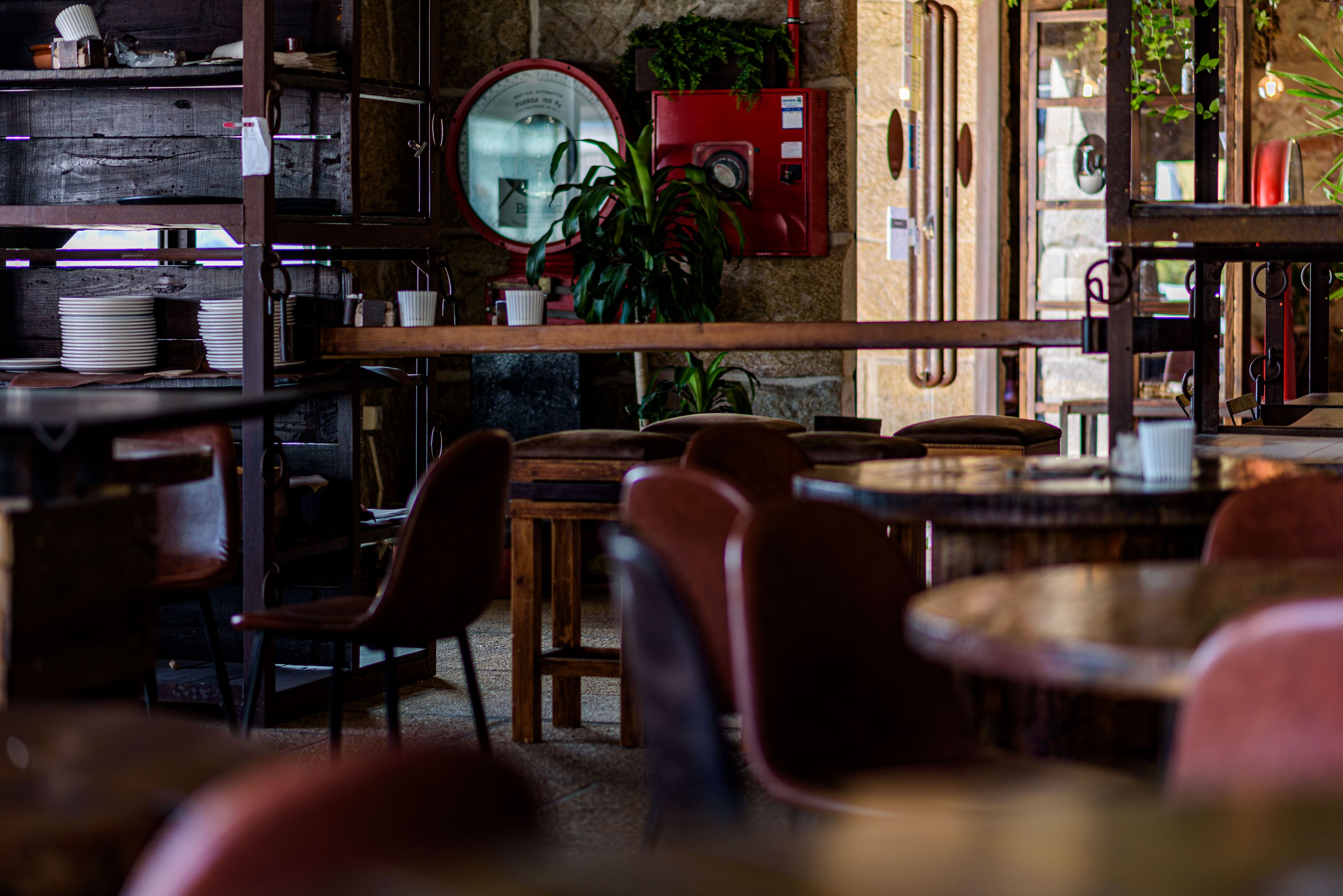 Interior acogedor de restaurante con mesas y sillas de madera, un cuadro eléctrico rojo y un espejo grande en la pared.